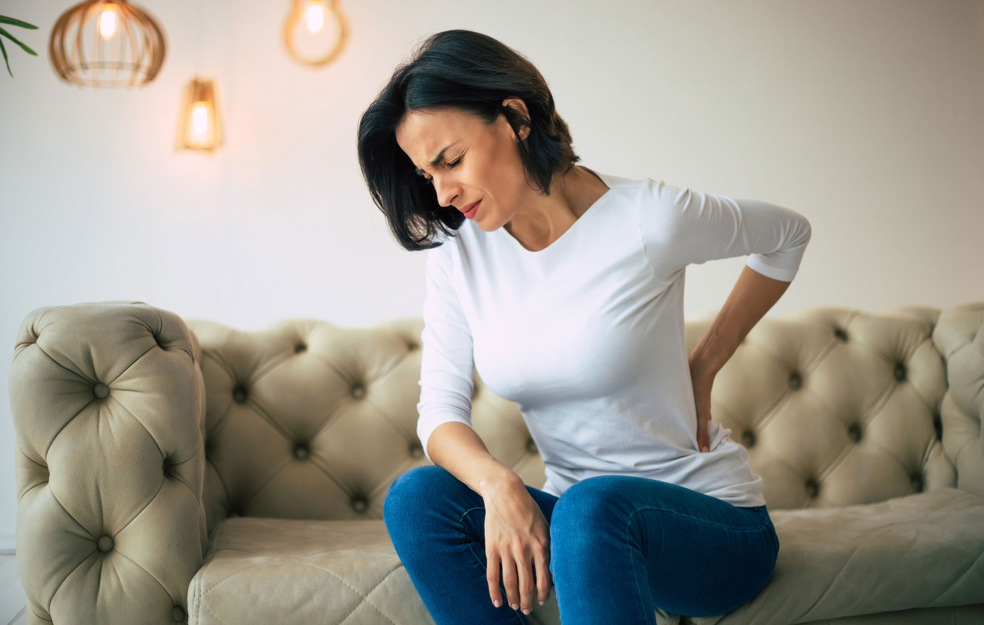 chronische Rückenschmerzen Frau sitzend auf Sofa